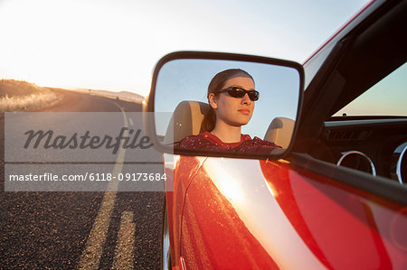 A young Caucasian woman reflected in side mirror of a convertible sports car on the highway.