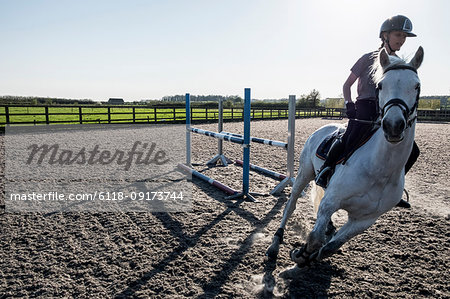 Teenage girl riding on a white horse in a paddock, taking a corner, horse moving at speed.