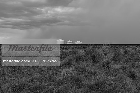 Grain silos and storm clouds over vast farmland and prairie, train tracks in foreground