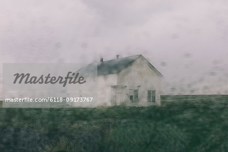 Abandoned farmhouse in a rainstorm, seen through a wet window. Blurred image.