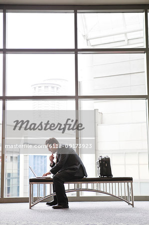 A businessman working on a laptop computer on a bench in a convention centre lobby