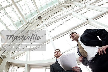 Two businessmen going over paperwork in the lobby of a large convention centre.