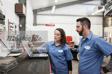 Two mechanics working on a laptop computer in a repair shop.