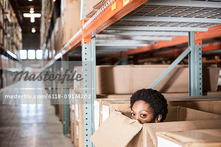 A black female worker hiding inside a cardboard box in a distribution warehouse.