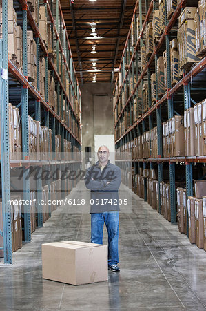 A black warehouse worker standing near boxed products in a distribution warehouse.