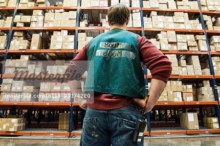 A view from behind a warehouse worker who is  checking inventory on the storage racks in a distribution warehouse.