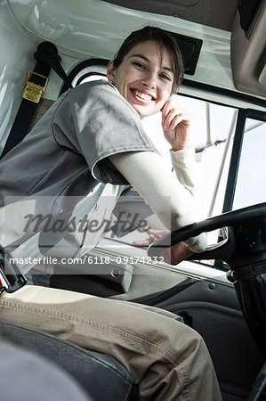 Portrait of a uniformed Caucasian female truck driver at the wheel of her truck at a distribution warehouse.