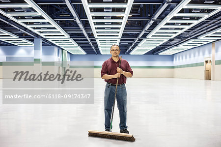 An Hispanic man standing with a broom in a large convention cener space.