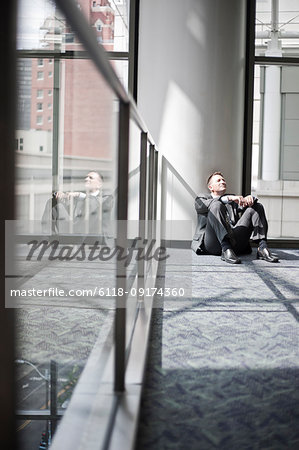 Low view looking at a Caucasian businessman taking a break sitting at the base of a column in a convention centre space.