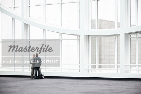 Two businessmen standing in a glassed in lobby area of a convention centre.