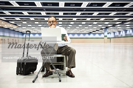 A Hispanic businessman looking at a laptop computer sitting at a small desk in the middle of a convention arena.