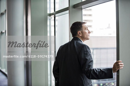 A Caucasian businessman standing next to and looking out of a large window in a convention centre.