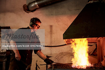 An artisan metal worker heating metal in a forge in his workshop.