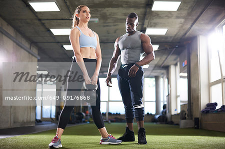 Trainer watching female client exercise with kettlebell in gym