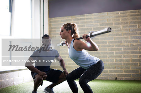 Trainer watching female client do squats with barbell in gym