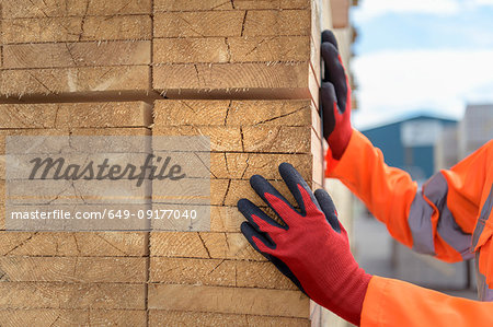 Worker inspecting stacks of timber in storage at port