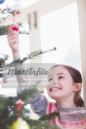 Smiling, curious girl touching ornament on Christmas tree