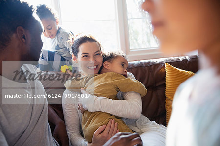 Happy mother cuddling baby son, relaxing with family on living room sofa