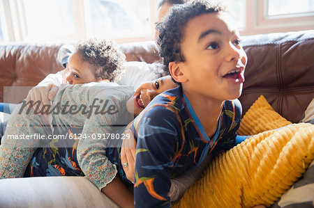 Playful, affectionate young family in pajamas on living room sofa