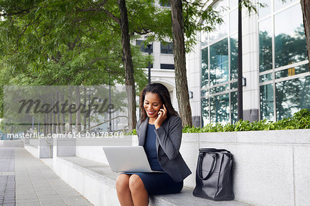Businesswoman using cellphone and laptop on street seating
