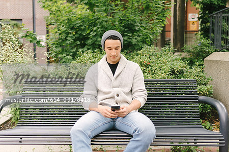 Young man texting while sitting on bench, Vancouver, Canada