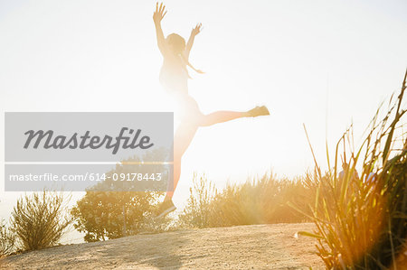 Woman jumping into air on hilltop