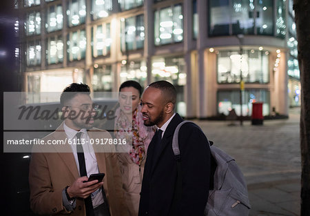 Business people with smart phone talking on city street at night