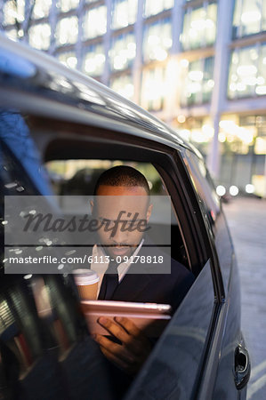 Businessman drinking coffee, using digital tablet in crowdsourced taxi