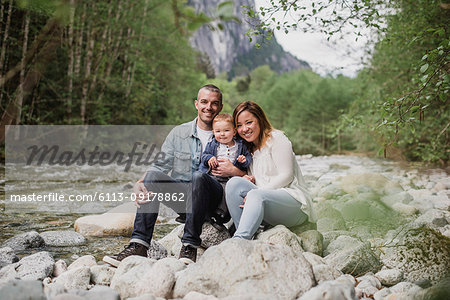 Portrait parents and baby son sitting on rocks at riverside