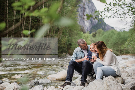 Parents and baby son sitting on rocks along stream
