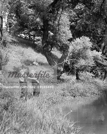 1930s TWO BOYS FISHING WITH STICK AND STRING FISHING RODS ON BRIGHT SUMMER DAY