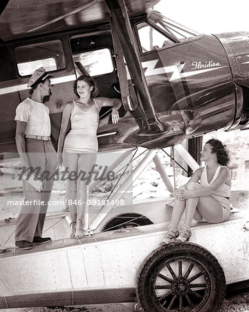 1930s TWO WOMEN IN BATHING SUITS WITH MALE PILOT OF AN AMPHIBIOUS AIRPLANE ON A FLORIDA BEACH