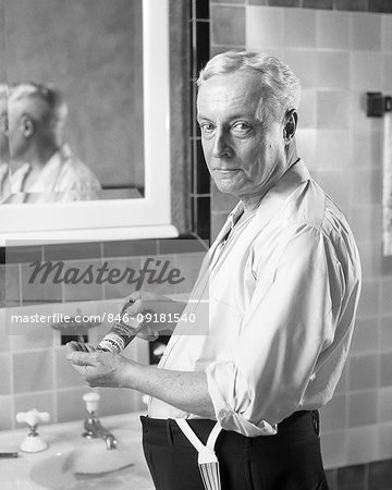 1920s SENIOR MAN STANDING IN SHIRT SLEEVES AT BATHROOM  SINK LOOKING AT CAMERA SQUEEZING GROOMING PRODUCT FROM TUBE INTO HAND