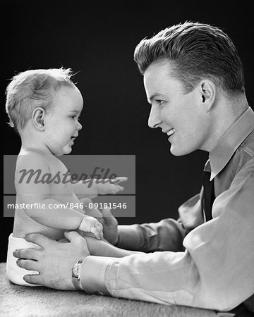1940s SMILING YOUNG MAN FACE TO FACE EYE TO EYE LOOKING AT YEAR OLD BABY GIRL DAUGHTER SITTING UP