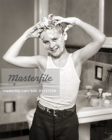 1930s SMILING BOY SHAMPOOING HIS HAIR STANDING LOOKING AT THE CAMERA