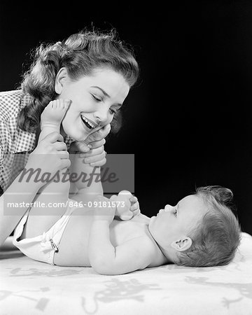 1940s MOTHER PLAYING WITH BABY GIRL HOLDING BABY'S LEGS UP TO TOUCH MOM'S FACE