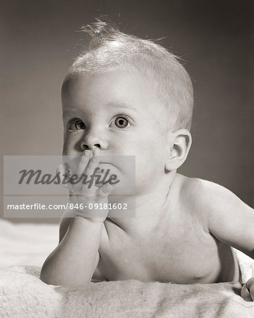 1960s PENSIVE FIVE MONTH OLD BABY LYING ON STOMACH LEANING CHIN IN HAND 1960s PENSIVE FIVE MONTH OLD BABY LYING ON STOMACH LEANING CHIN IN HAND