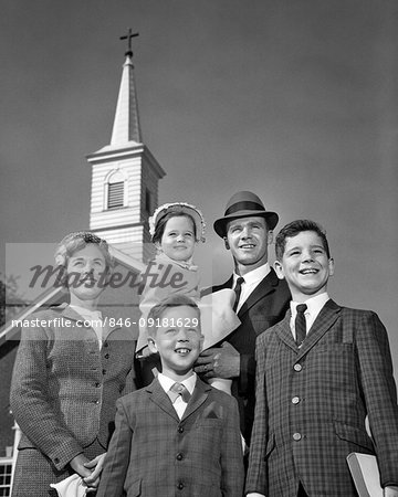 1960s FAMILY PORTRAIT MOTHER FATHER TWO SONS ONE DAUGHTER IN ARMS CHRISTIAN CHURCH SPIRE BEHIND THEM