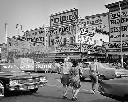 1970s PEDESTRIANS CROSSING STREET TO NATHAN'S HOT DOG STAND AT CONEY ISLAND BEACH NY USA