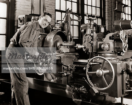 1940s SMILING MAN WORKING A LATHE MACHINE IN A FACTORY LOOKING AT CAMERA