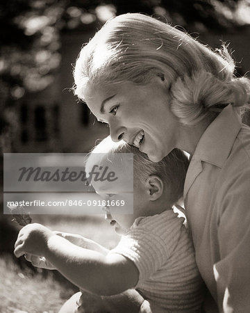 1960s SMILING BLOND MOTHER HOLDING CHILD WITH LEAF