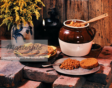 1950s COLONIAL AMERICAN DISH CERAMIC CROCK POT OF BOSTON BAKED BEANS SERVED ON PEWTER PLATE WITH SLICE OF BOSTON BROWN BREAD