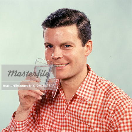 1960s SMILING MAN WEARING RED CHECKED SHIRT LOOKING AT CAMERA DRINKING GLASS OF WATER
