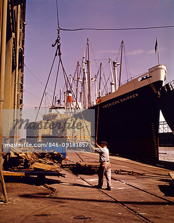 1950s WHARF SIDE INDIVIDUAL PALLETS OF FREIGHT BEING LOADING ON TO OR UNLOADING OFF FROM A TRAMP STEAMER OCEAN GOING FREIGHTER