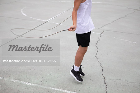 Male teenage basketball player on basketball court skipping, neck down