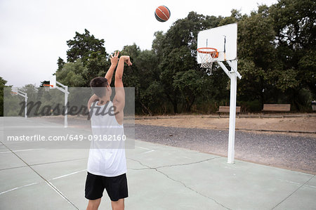 Male teenage basketball player throwing ball toward basketball hoop