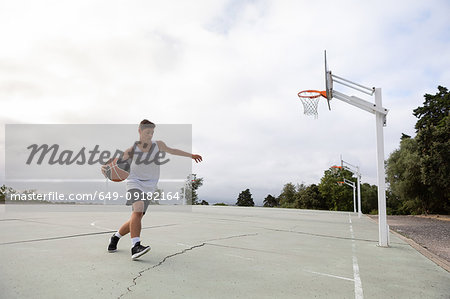 Male teenage basketball player running with ball on basketball court