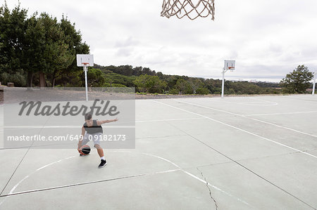 Male teenage basketball player practicing with ball near basketball hoop