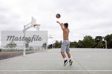 Male teenage basketball player jumping and throwing ball toward basketball hoop
