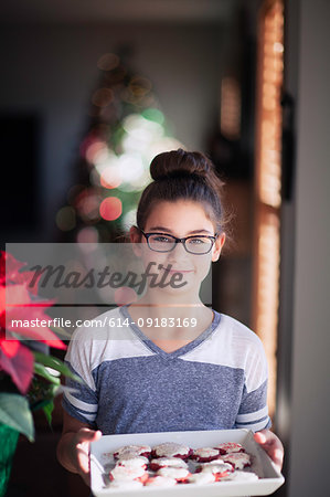 Girl holding tray of homemade christmas cookies in living room, portrait